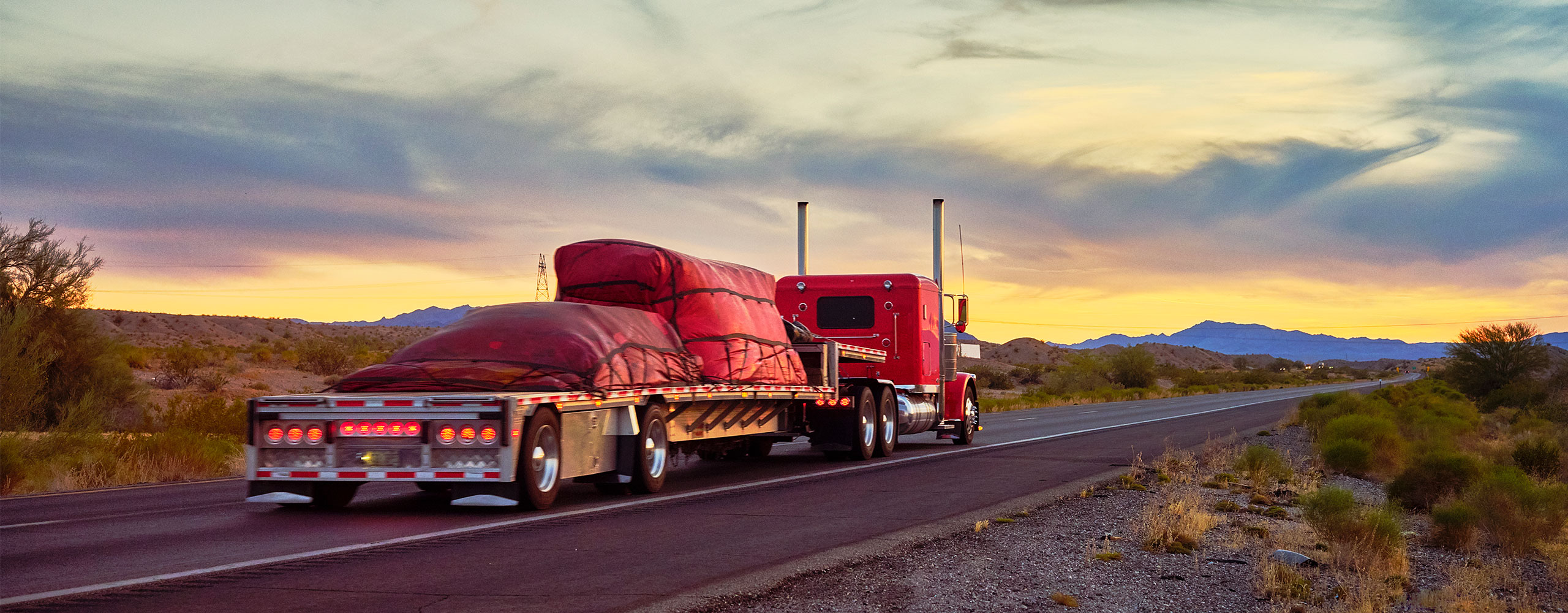 Red flatbed truck carrying freight on highway in front of North American landscape